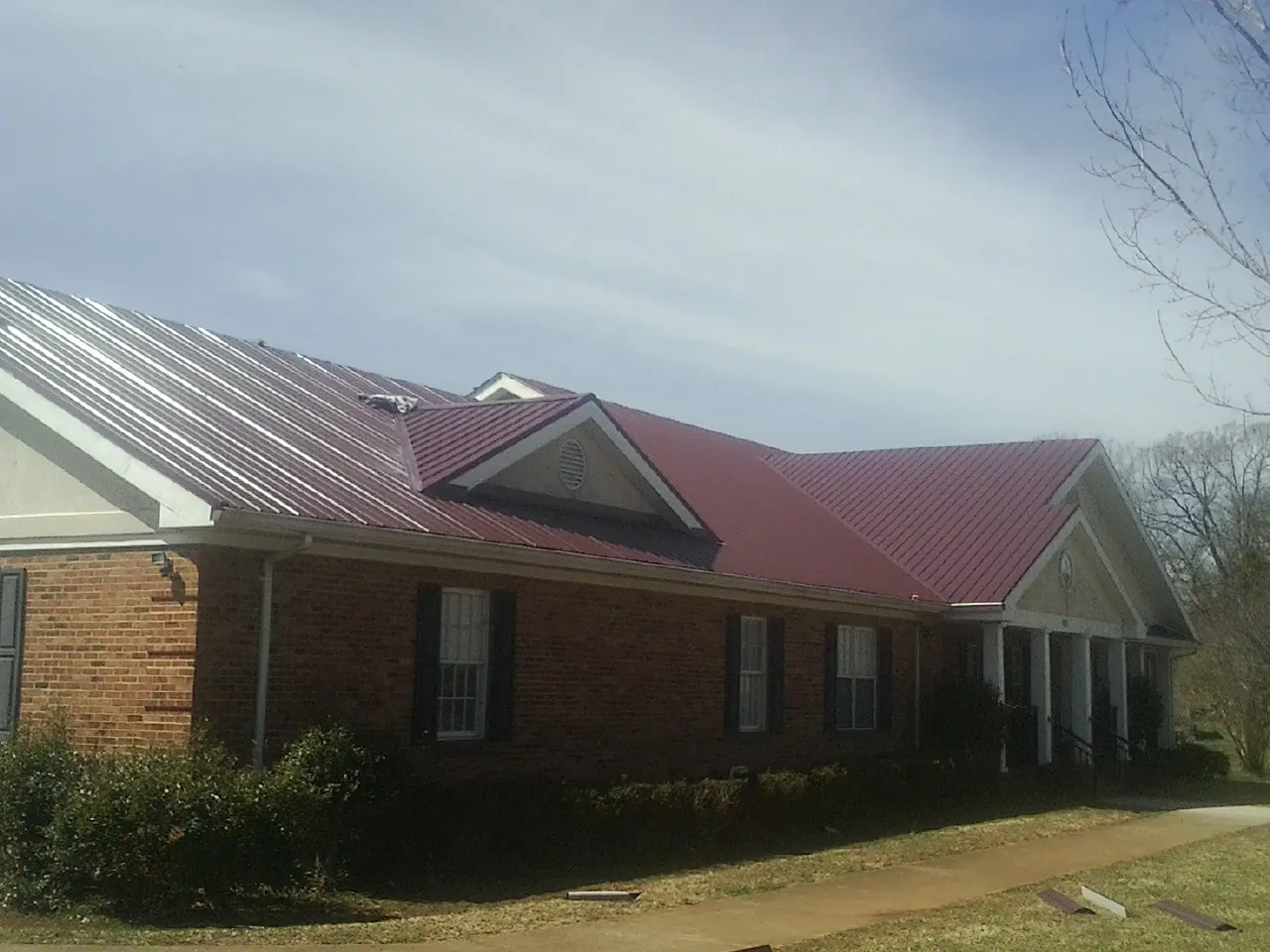 Red metal roof with gabled entries on a long brick building, from a Hail Damage Roof Repair job in Sarasota