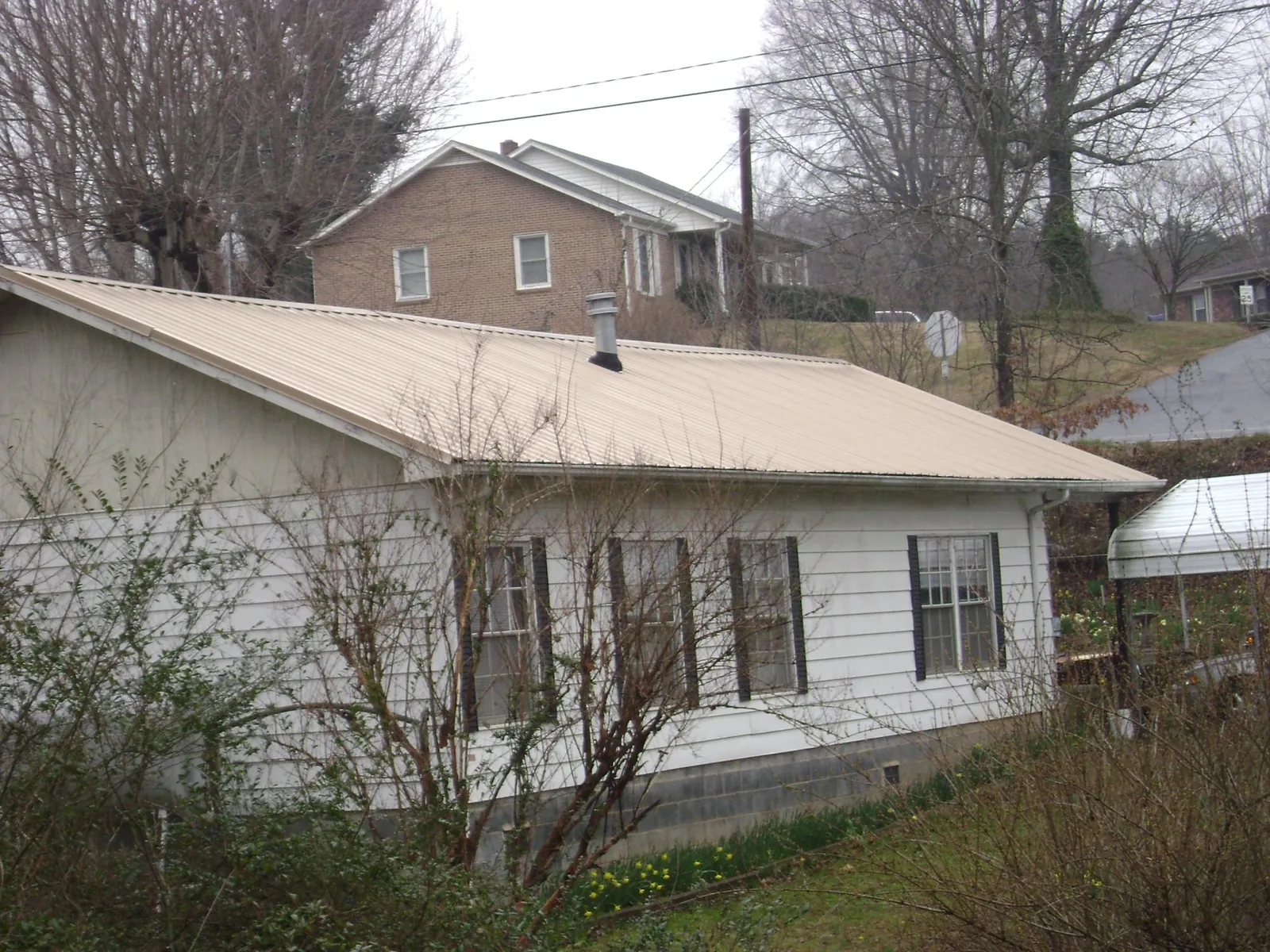 Tan metal roof on a white sided house set into a hillside — Commercial Roofing by Roofing Brothers in Sarasota